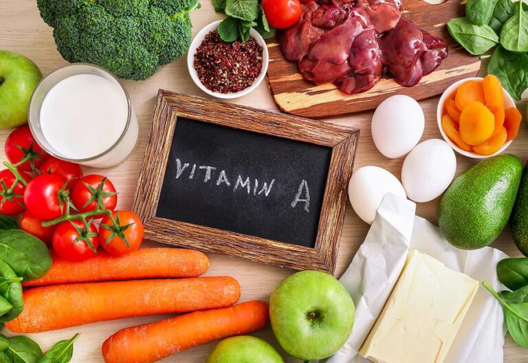 Vitamin A-rich foods arranged around chalkboard: carrots, liver, eggs, tomatoes, broccoli, and dairy products