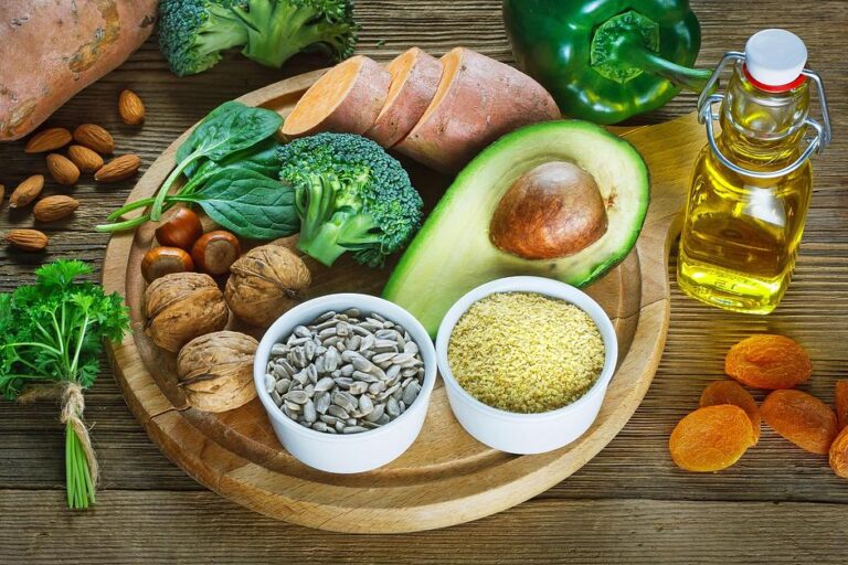 Foods rich in Vitamin E including nuts, seeds, avocado, sweet potato, and olive oil on wooden board