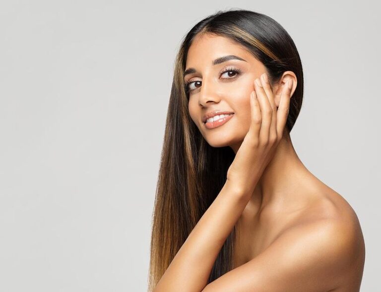 Radiant beauty with glowing skin, sleek ombre hair, and manicured nails touching face gently from biotin
