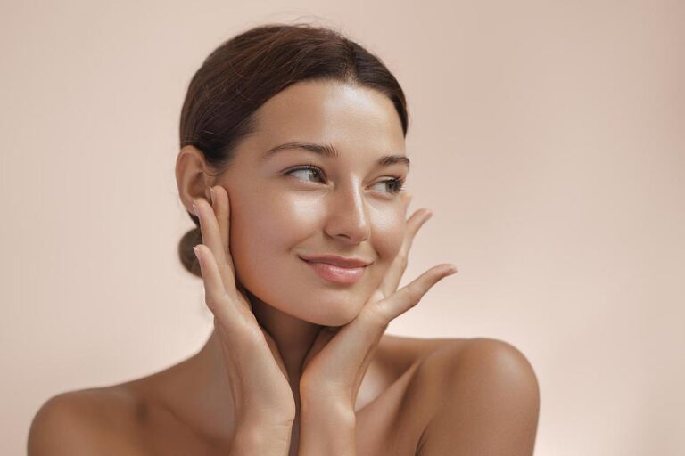 Close-up of glowing, healthy skin with natural radiance as hands gently touch face from niacinamide against neutral background.